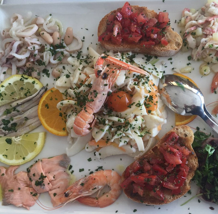 Antipasto di mare con scampo, gamberi, insalata di seppia, alici marinate, salmone, bruschette al pomodoro e limone
