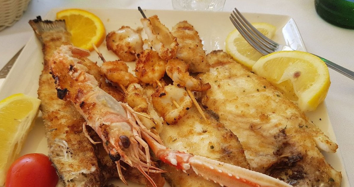 Pesce gratinato alla griglia con scampo, spiedini di calamari e limone su piatto bianco del Ristorante da Giuseppe